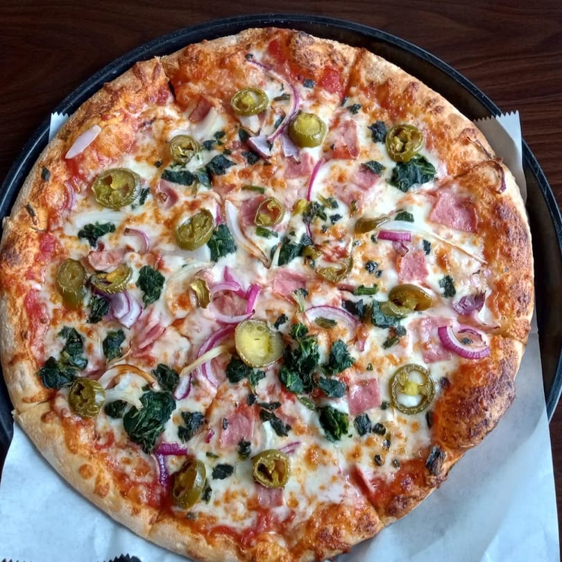 Basil's Pizza with ham, red onions, jalapeños, and spinach on a dark pan.