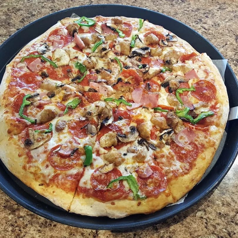 Basil's Pizza with pepperoni, ham, sausage, mushrooms, and green peppers on a black tray.