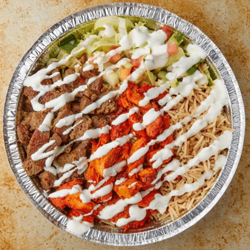 A foil container filled with rice, chicken, beef, lettuce, tomatoes, and white sauce.