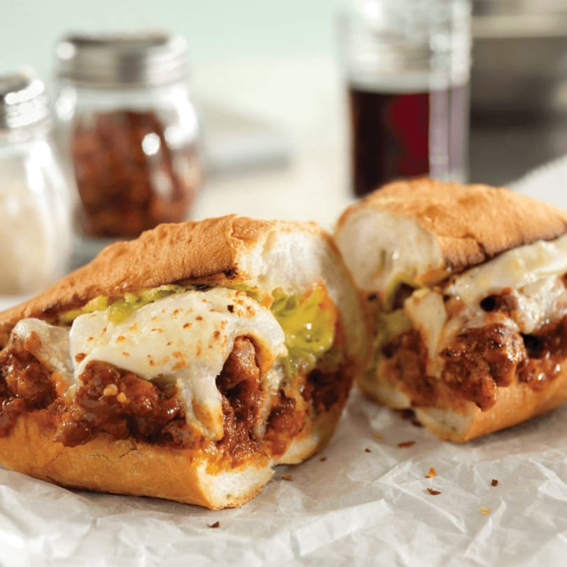 Two halves of a meatball sub with melted cheese and green peppers on white paper.