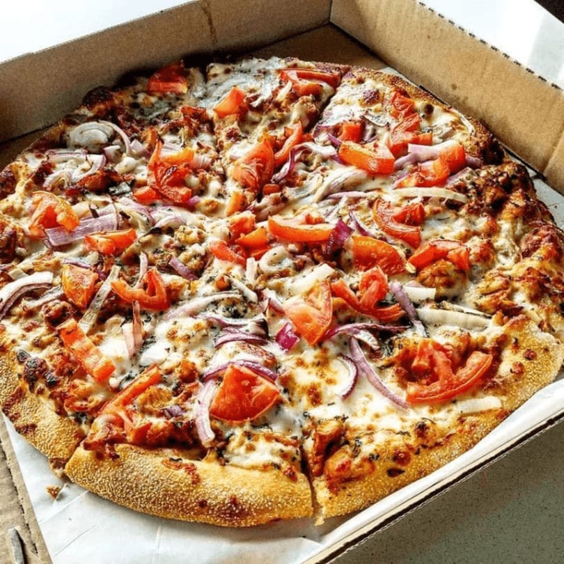 A whole Basil's Pizza with tomatoes, red onions, and chicken in a cardboard box.
